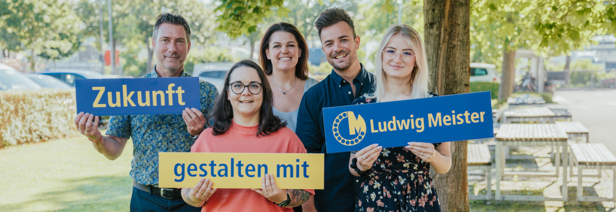 Fünf Personen halten Schilder mit der Aufschrift "Zukunft gestalten mit Ludwig Meister" in einem parkähnlichen Umfeld.