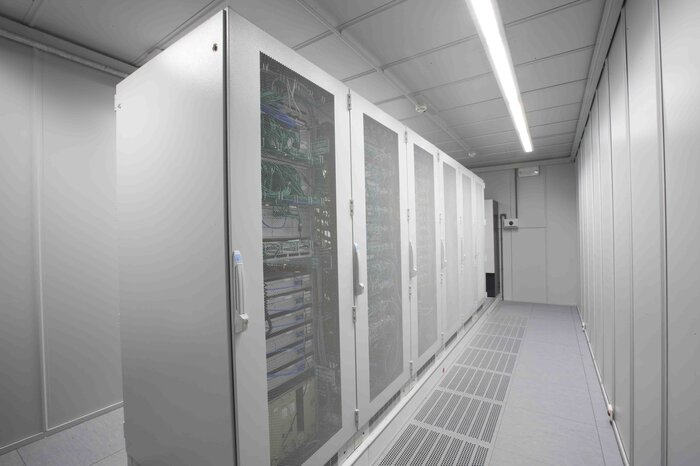 Ein langer Gang in einem Serverraum mit mehreren weißen Server-Schränken und einer klaren Beleuchtung von der Decke.