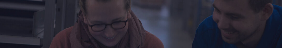 Zwei fröhliche Personen schauen zusammen auf ein Dokument in einem Lagerraum.